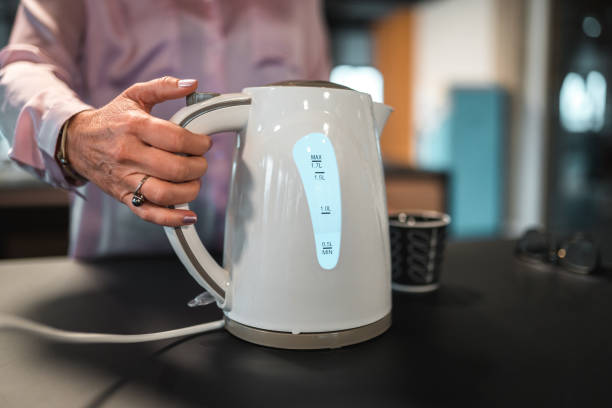 Close-up nas mãos de uma funcionária caucasiana preparando uma xícara de chá no trabalho. Boling uma água em uma chaleira elétrica.