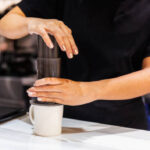 Método de preparo do café com sistema Aero Press. Mulher barista de camiseta preta pressiona Aeropress para encher um copo com café expresso no balcão de mármore. Café profissional para fazer café.