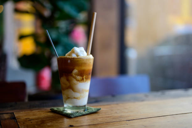 Foto de café gelado doce e cremoso com leite de coco em um copo alto na mesa de madeira.