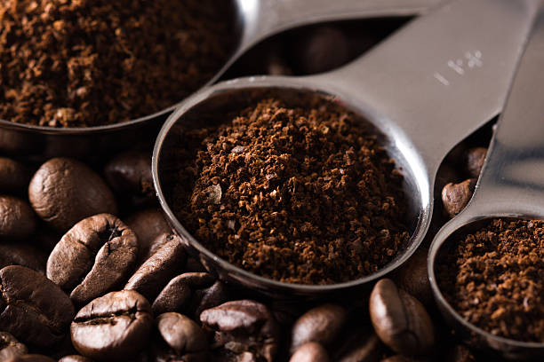 Colheres medidoras com café moído e grãos de café.