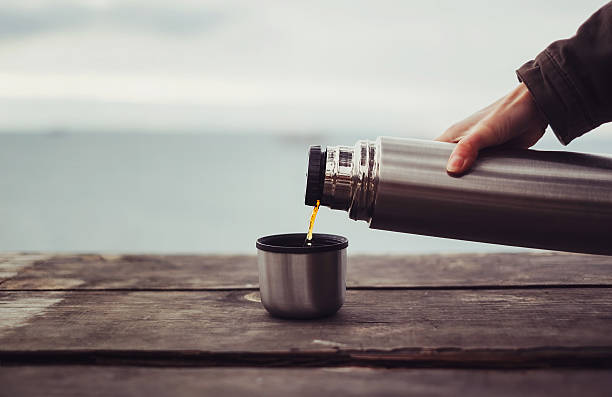 Viajante irreconhecível derramando chá em uma xícara de garrafa térmica na mesa de madeira no fundo do mar. Tema turismo e viagens
